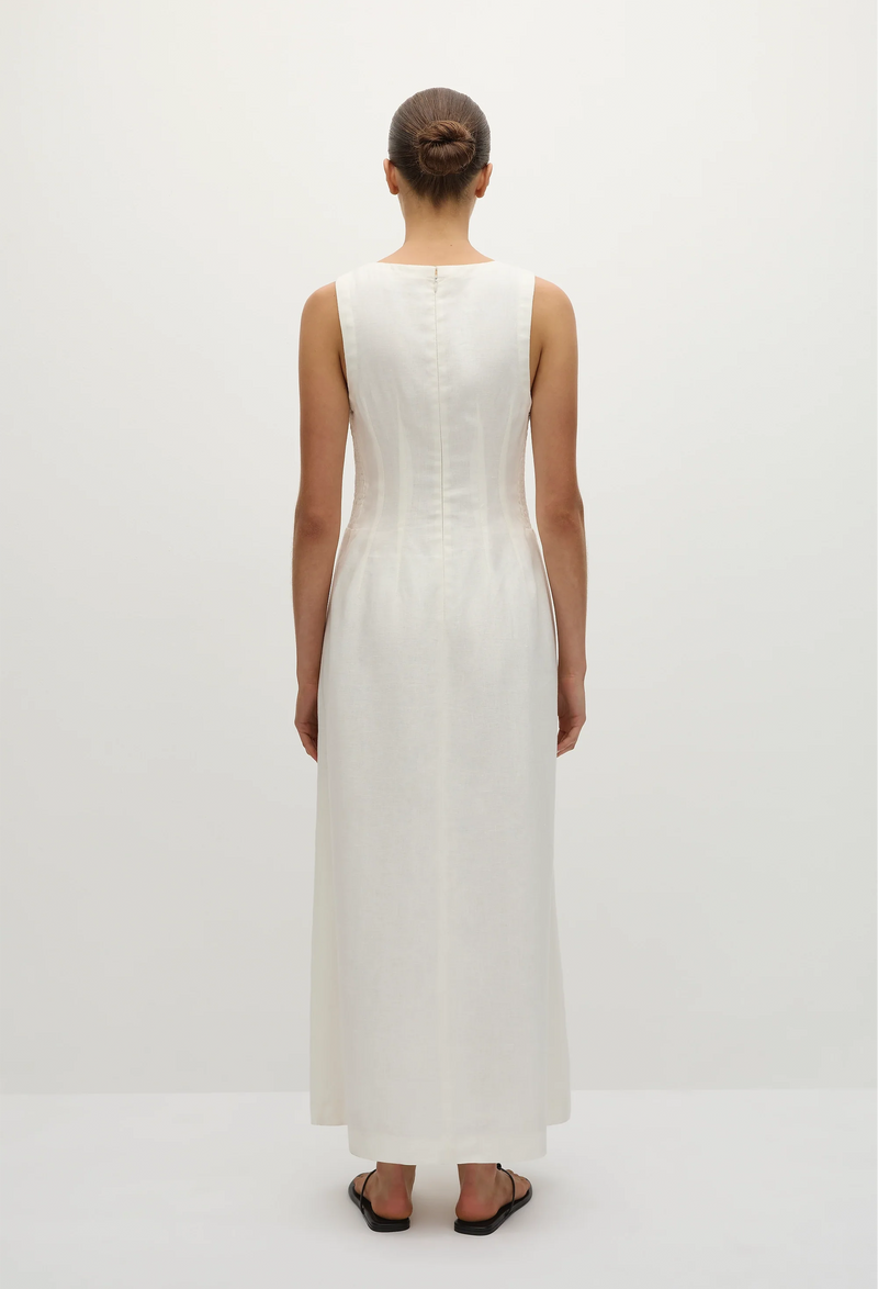 the back of a model wearing a sleeveless deep v-neck white maxi dress with a fitted bodice and slightly flared skirt. white background.