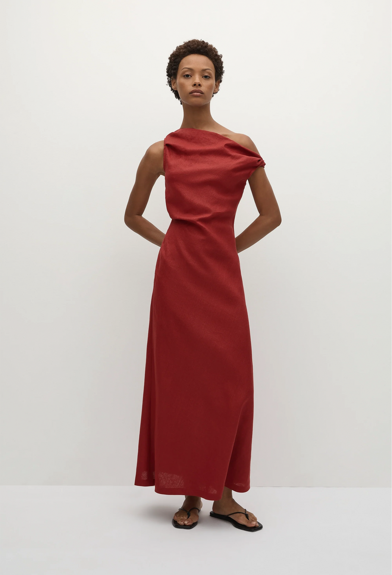 a model wearing a one-shoulder linen red maxi dress with one off the shoulder strap. white background.