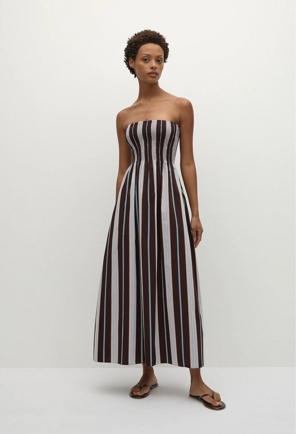 a model wearing a strapless maxi dress with blue and brown stripes. white background.