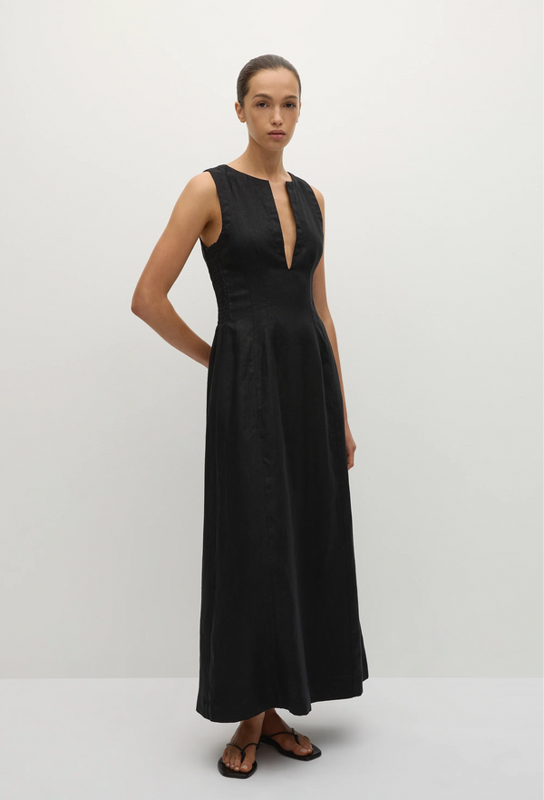 a model wearing a sleeveless deep v-neck black maxi dress with a fitted bodice and slightly flared skirt. white background.