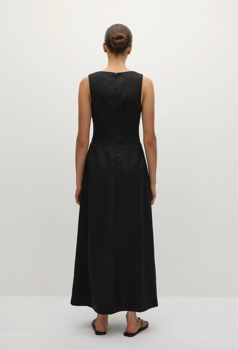 the back of a model wearing a sleeveless deep v-neck black maxi dress with a fitted bodice and slightly flared skirt. white background.