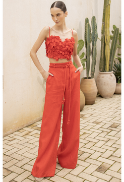 a model wearing high waisted red linen pants with a floral red crop top. image taken outside a building in front of cacti.