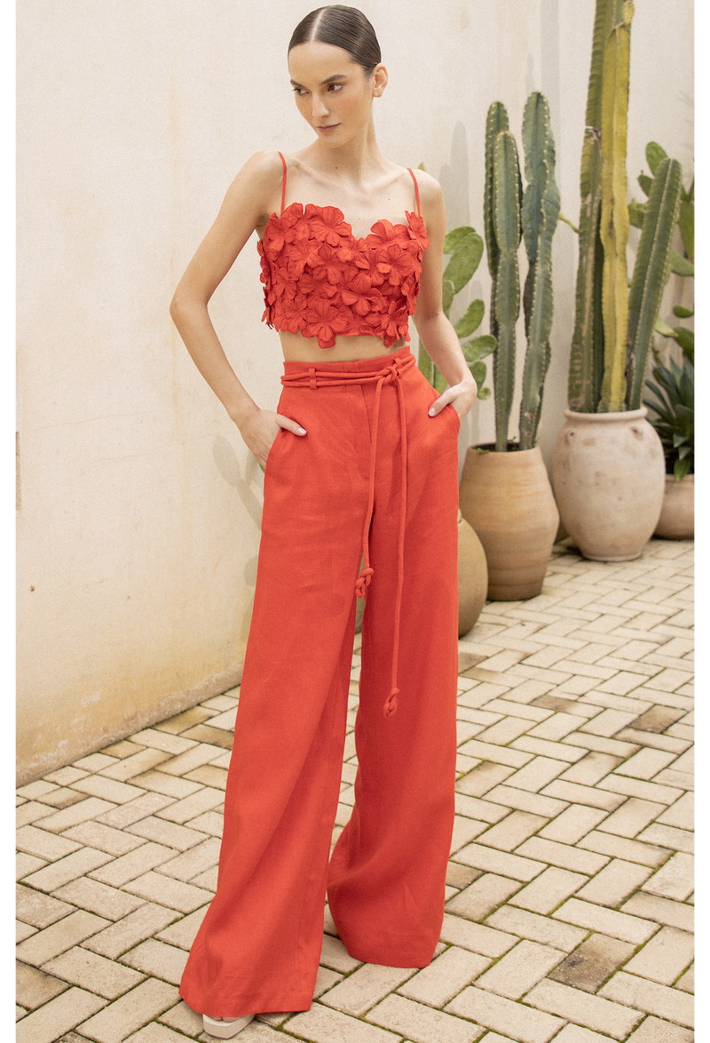 a model wearing high waisted red linen pants with a floral red crop top. image taken outside a building in front of cacti.