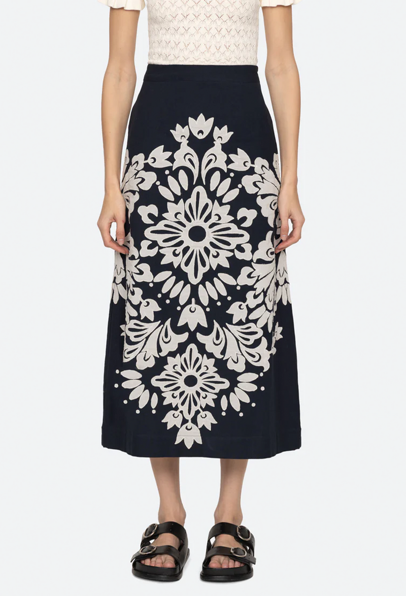 a model waring a navy midi skirt with a white design on it. white background