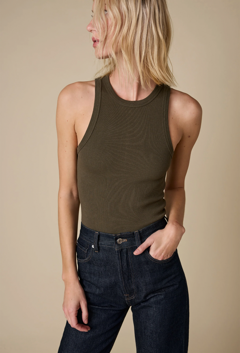 a model wearing an olive high neck racerback ribbed tank top and jeans. beige background