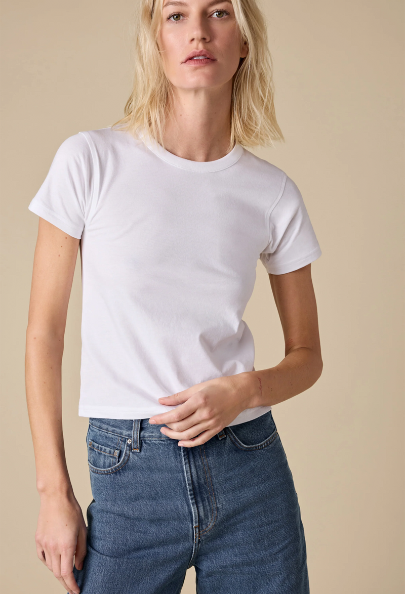 a model wearing a white shrunken t-shirt and jeans. beige background