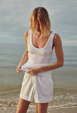 a model at the beach wearing white shorts and a scoop neck ribbed tank top.