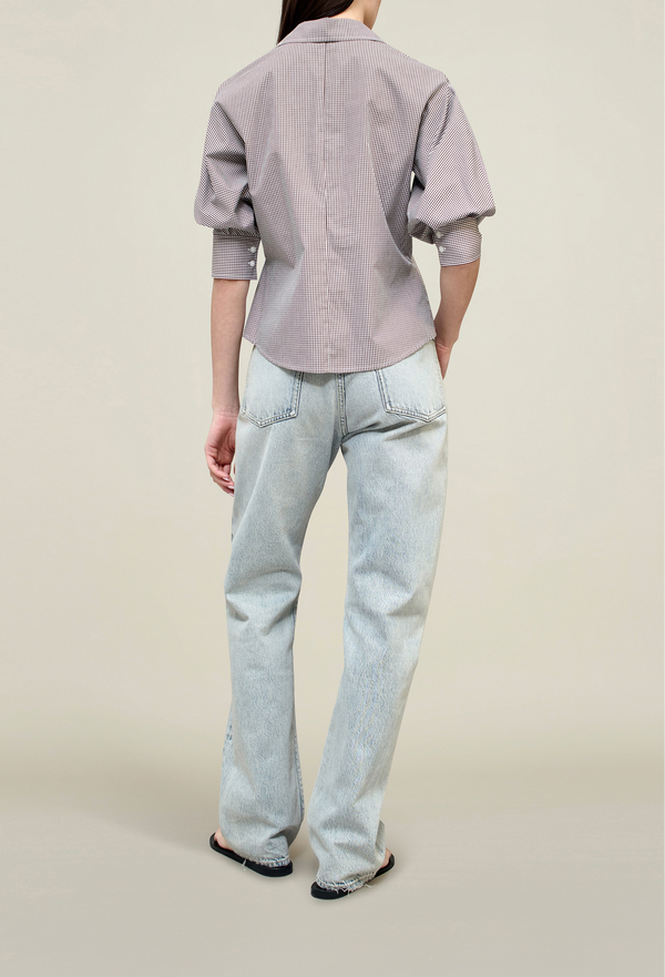 the back of a model wearing a brown gingham 3/4 puff sleeve button down top with jeans. tan background.