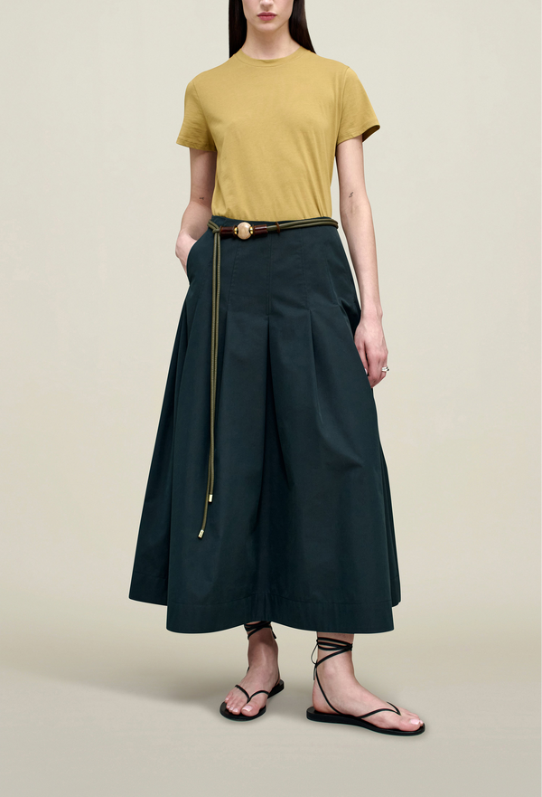 a model wearing a midi pleated navy skirt. tan background.