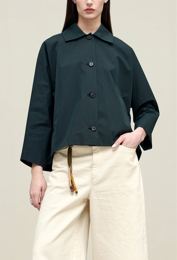 a model wearing a navy collared button down jacket. tan background.