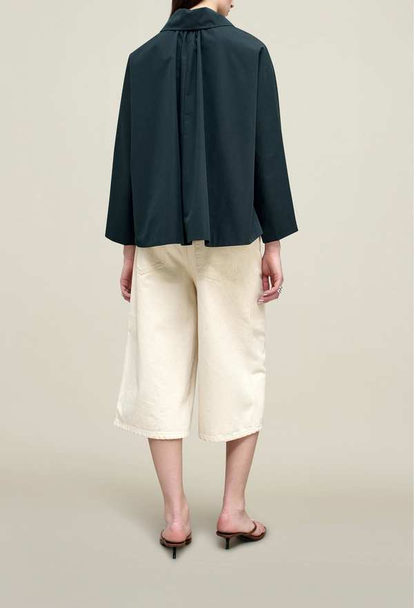the back of a model wearing a navy collared button down jacket. tan background.