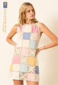 a model wearing a sleeveless multicolored pastel patchwork linen and crochet mini dress. white background
