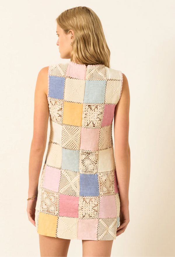 the back of a model wearing a sleeveless multicolored pastel patchwork linen and crochet mini dress. white background