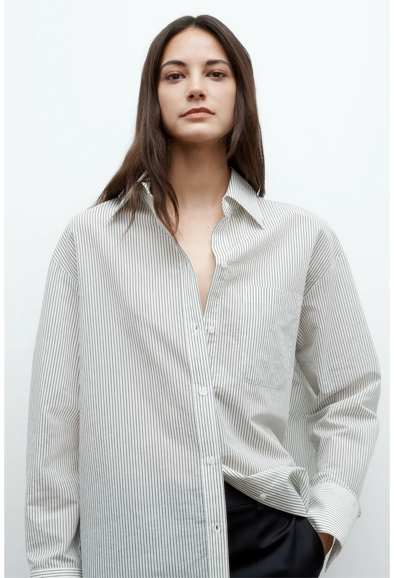 a model wearing an oversized white and dark green pinstripe collared button down shirt. white background