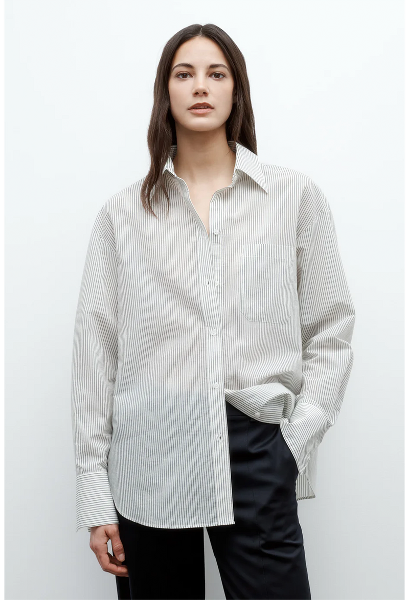 a model wearing an oversized white and dark green pinstripe collared button down shirt. white background