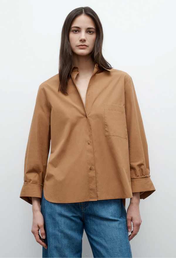 a model wearing a caramel brown button up long sleeve shirt with jeans. white background.