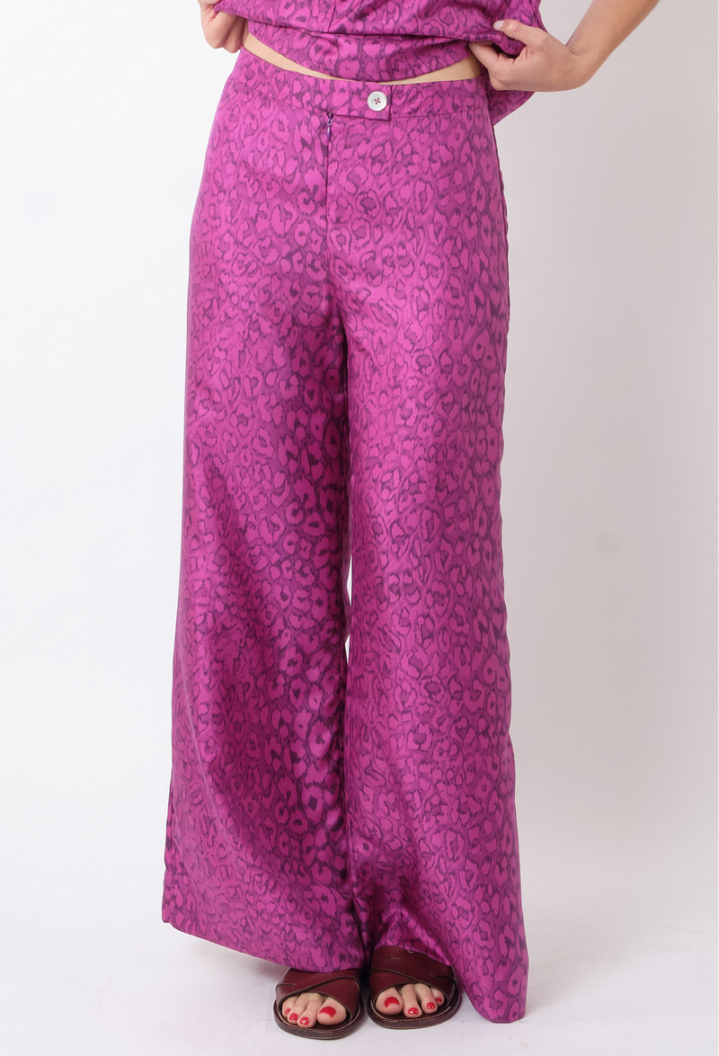 a model wearing a pair of purple panther print pants. white background.