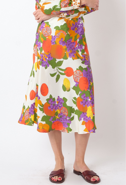 a model wearing a white midi skirt with multicolored fruit printed all over. white background.