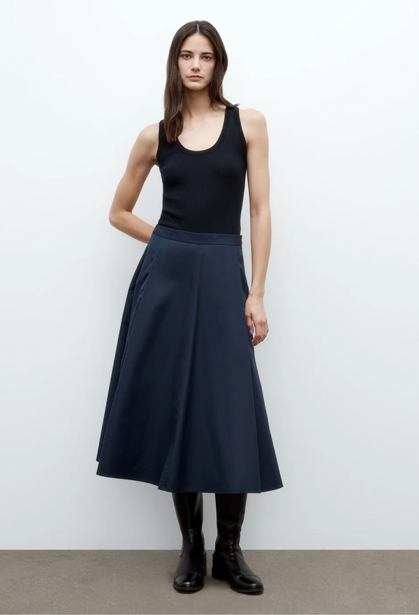 a model wearing a blue tank top and a navy midi skirt with pleats. white background.