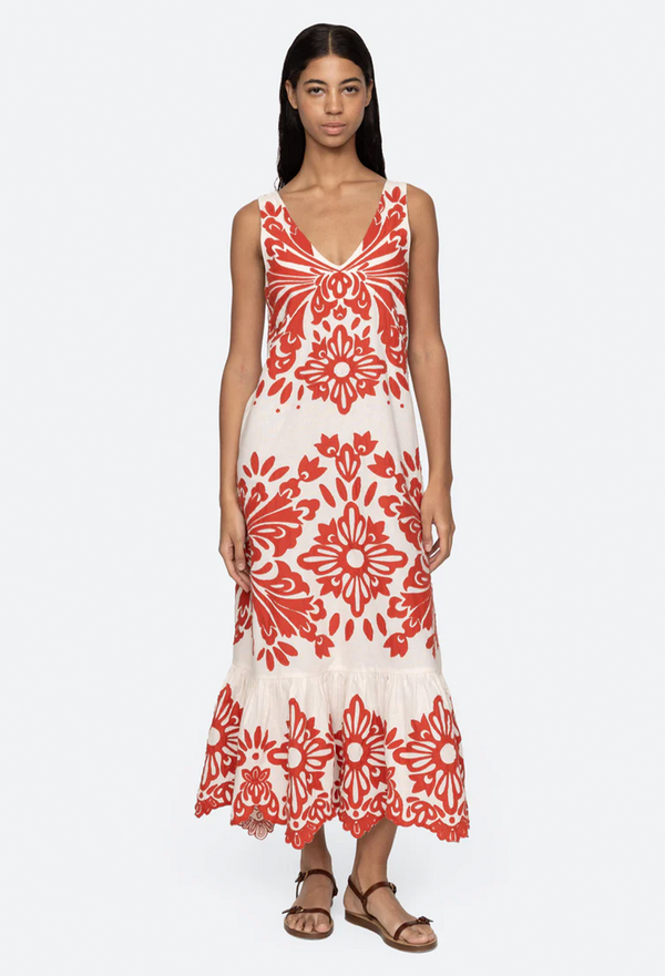 a model wearing a sleeveless v-neck white dress with red floral applique patterns on a white background