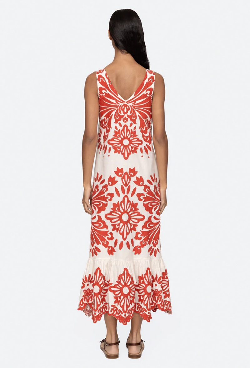 a model wearing a sleeveless v-neck white dress with red floral applique patterns on a white background