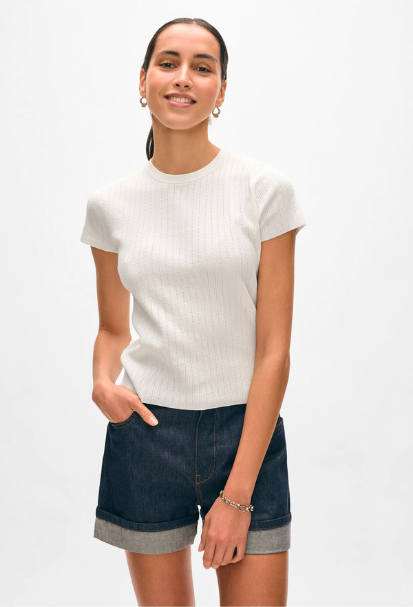 Woman wearing a white pointelle t-shirt and denim shorts on a white background