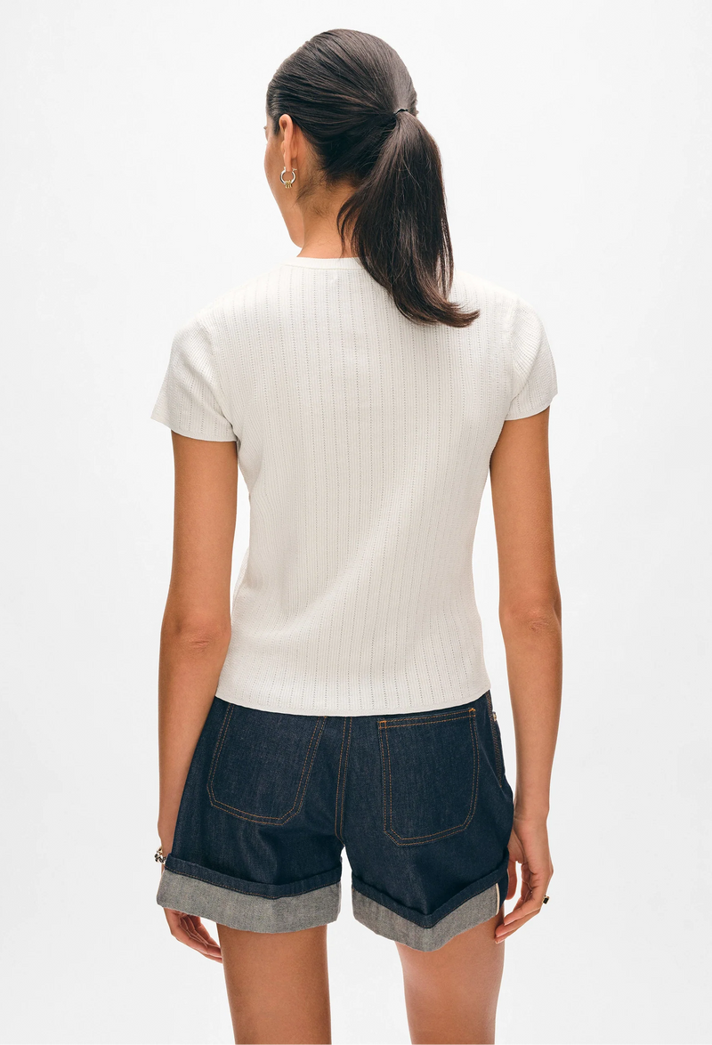 the back of a woman wearing a white pointelle t-shirt and denim shorts on a white background