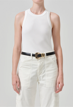 a model wearing an off white ribbed racerback tank top and white jeans. white background.