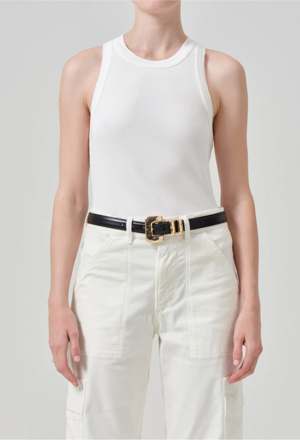 a model wearing an off white ribbed racerback tank top and white jeans. white background.
