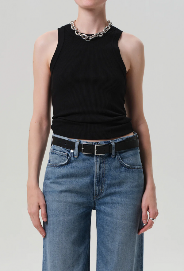 a model wearing a black ribbed racerback tank top and blue jeans. white background.