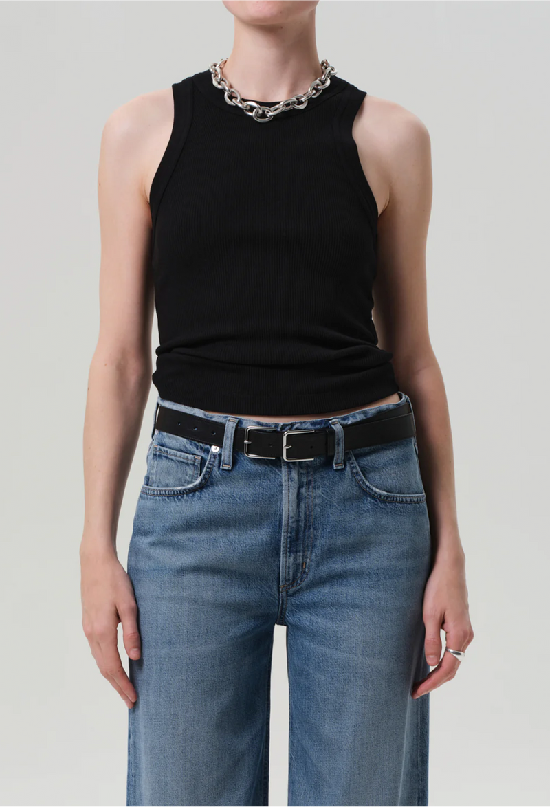 a model wearing a black ribbed racerback tank top and blue jeans. white background.