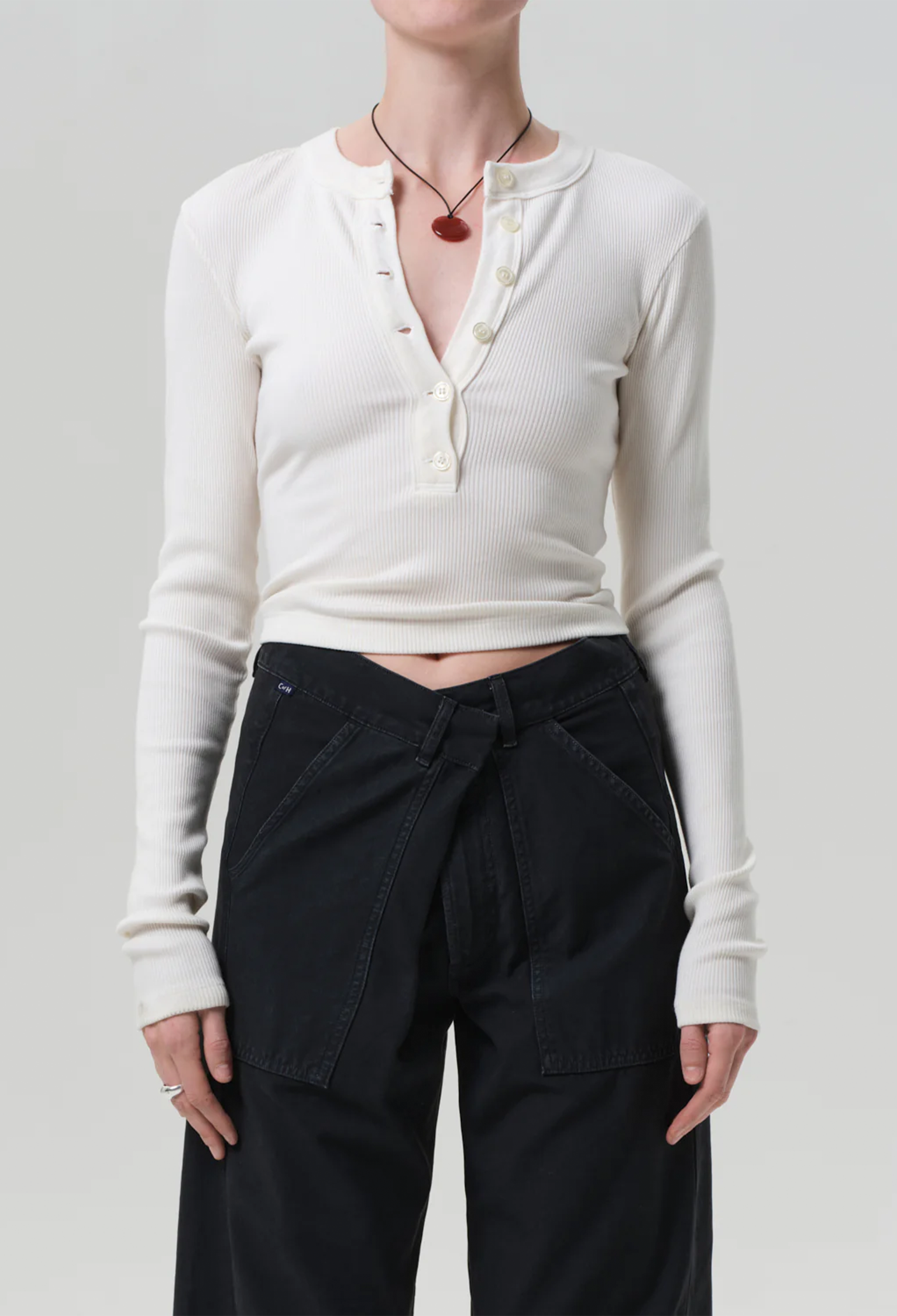 a model wearing an off white half buttoned henley long sleeve top with black jeans. white background.