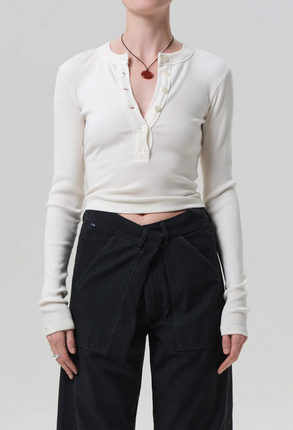 a model wearing an off white half buttoned henley long sleeve top with black jeans. white background.