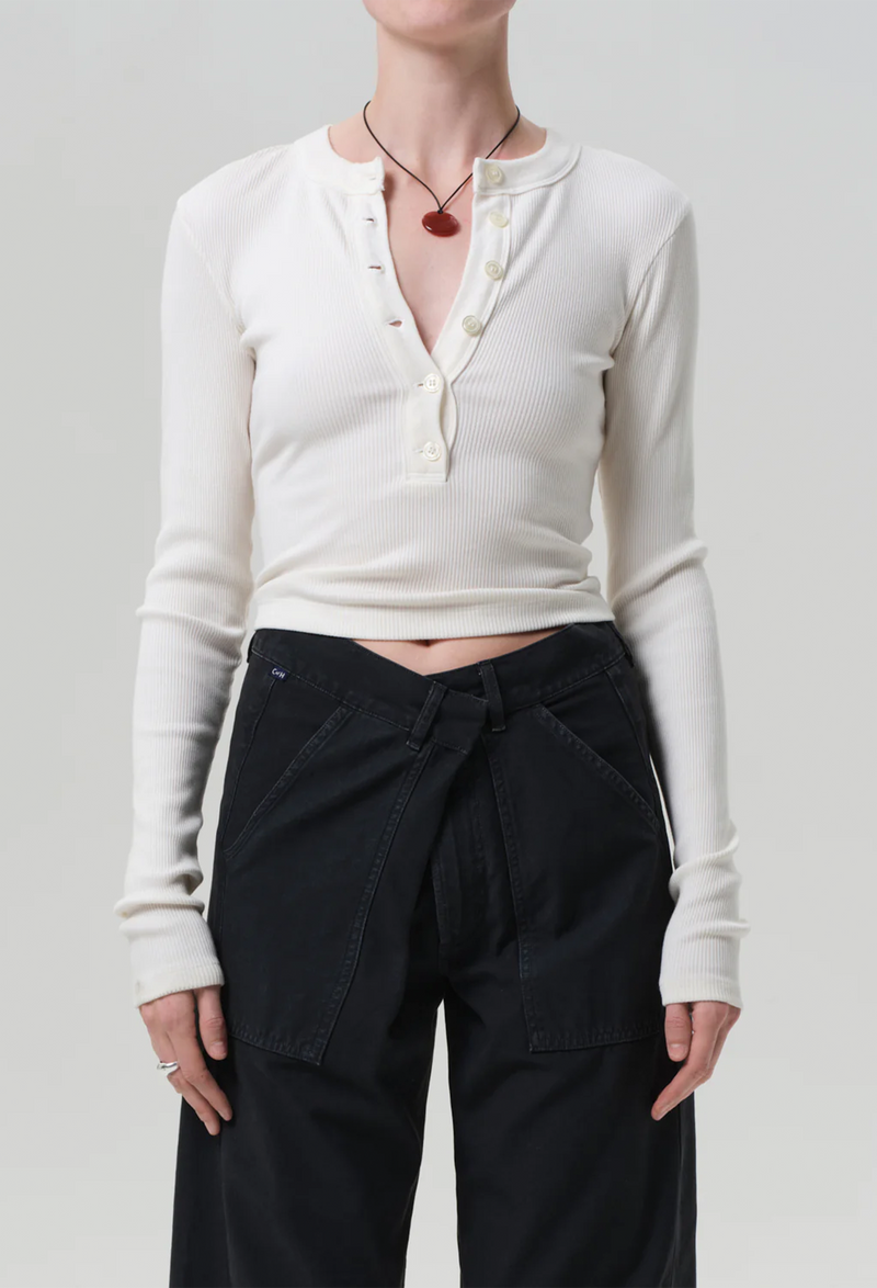 a model wearing an off white half buttoned henley long sleeve top with black jeans. white background.