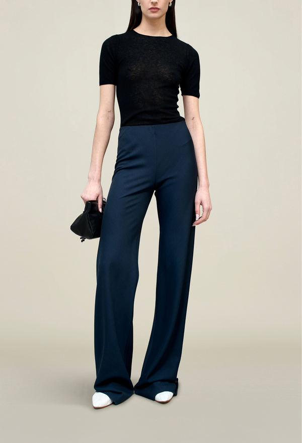 model wearing a black top and navy flare leg pants on a beige background