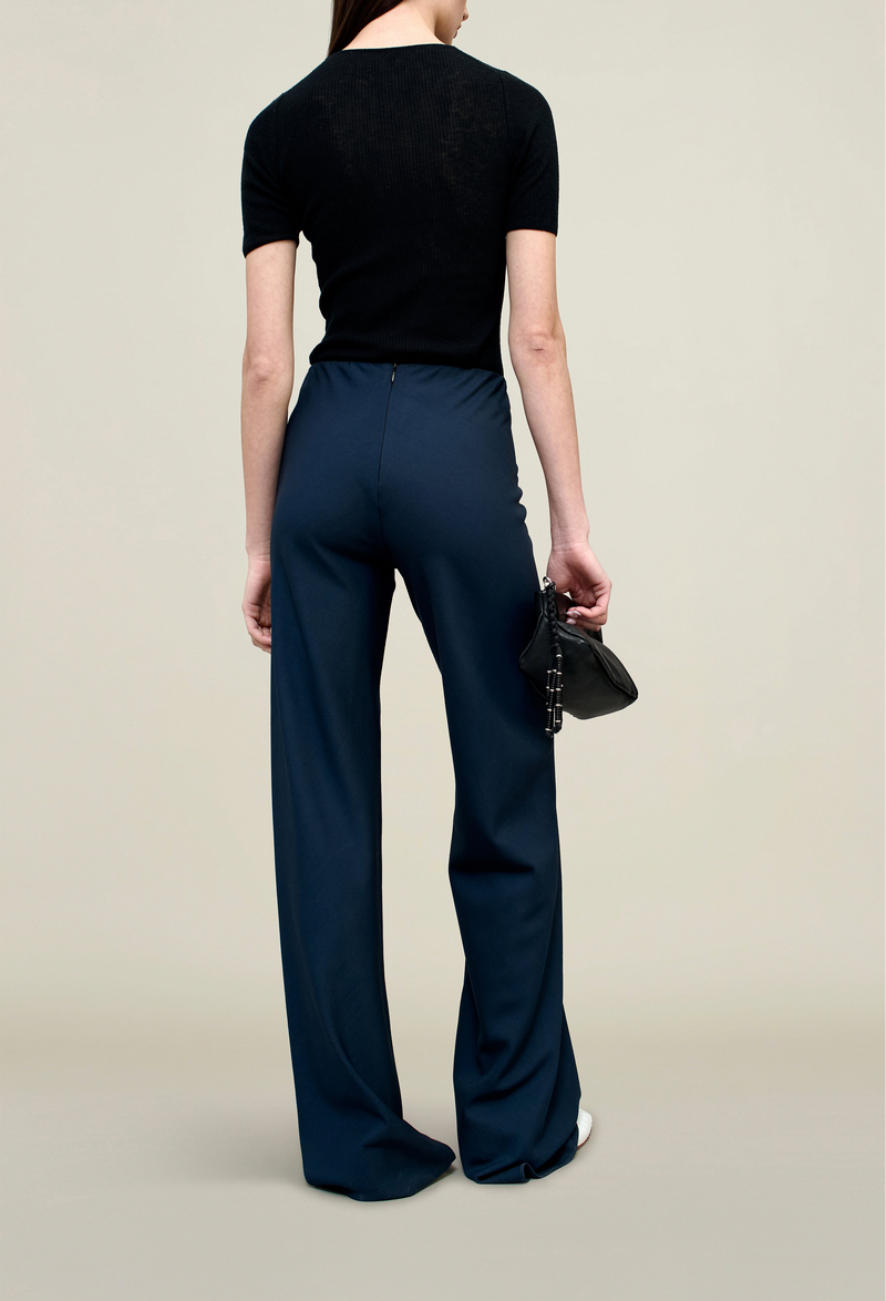 back of a model wearing a black top and navy flare leg pants on a beige background