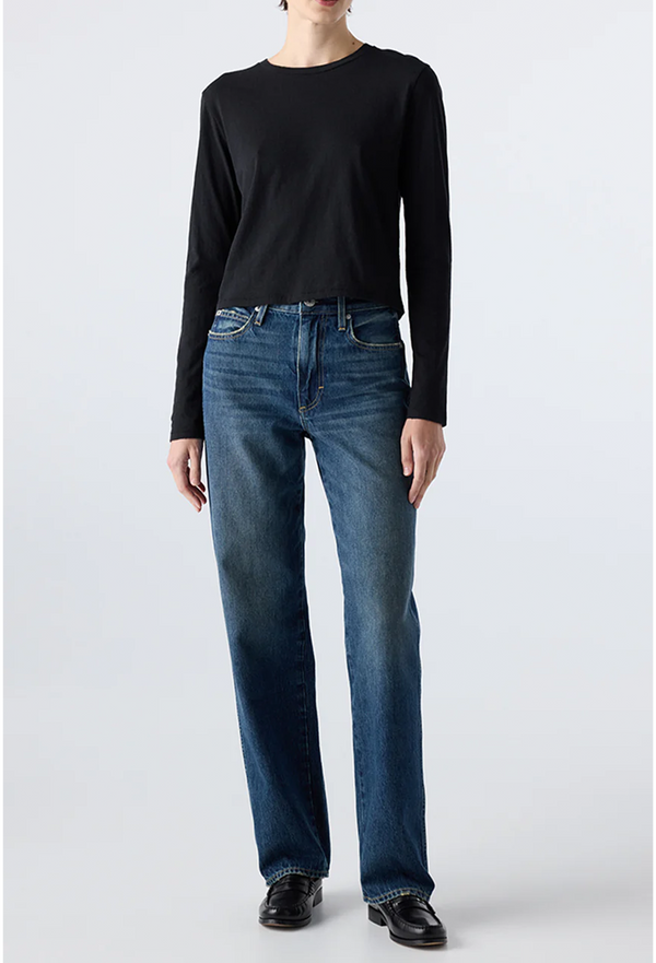model wearing a black long-sleeve shirt and dark blue jeans on a white background