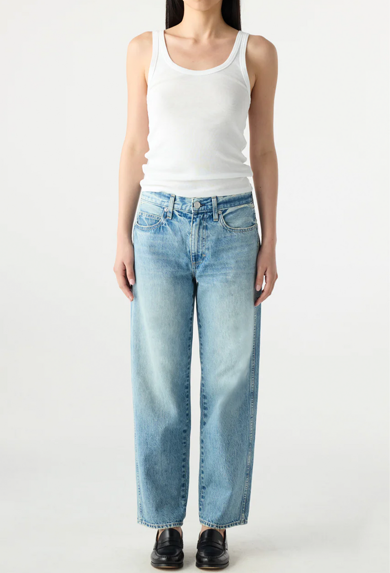 model wearing a white tank top and light blue jeans on a white background