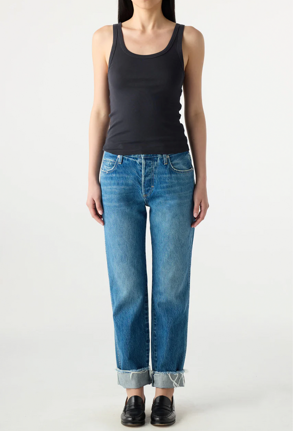 Person wearing a black tank top and cuffed blue jeans on a white background