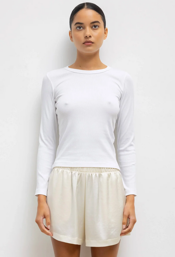 Woman wearing a white long-sleeve top and beige shorts against a plain background
