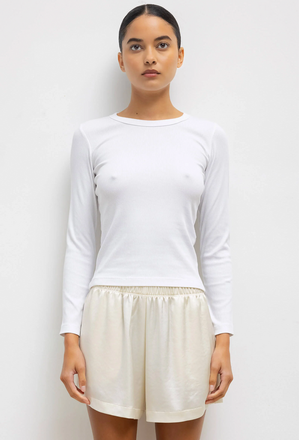 a model wearing a fitted white long sleeve tee and shorts on a white background.