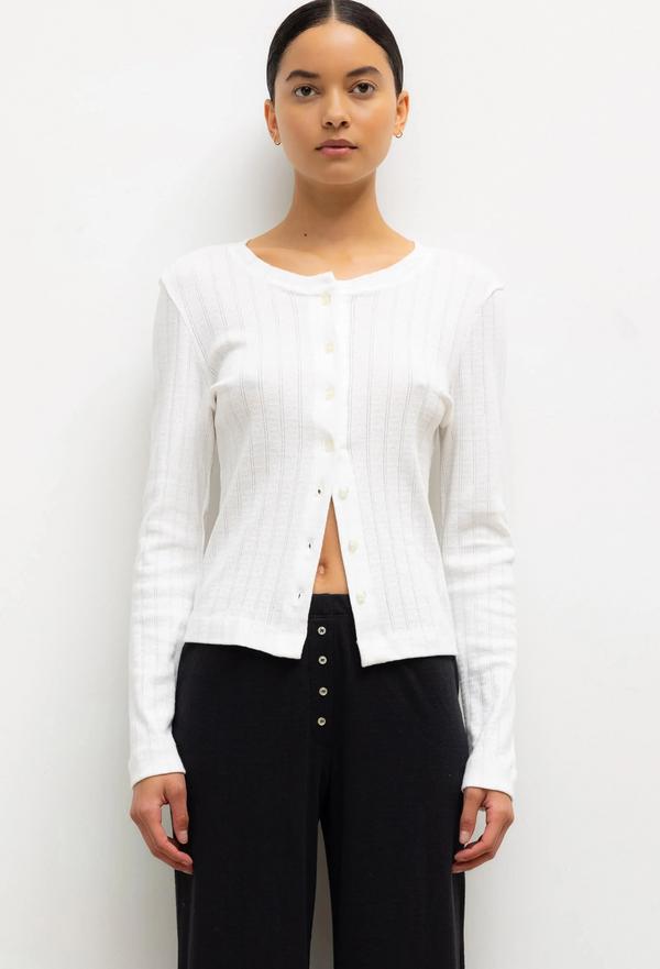 model wearing a white pointelle cardigan and black pants on a white background