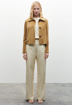 Woman wearing a tan jacket and beige pants against a white background