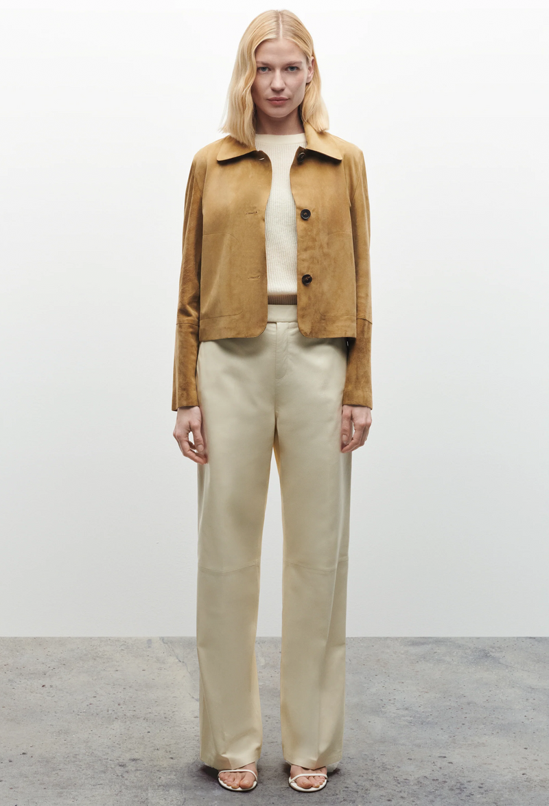 Woman wearing a tan jacket and beige pants against a white background