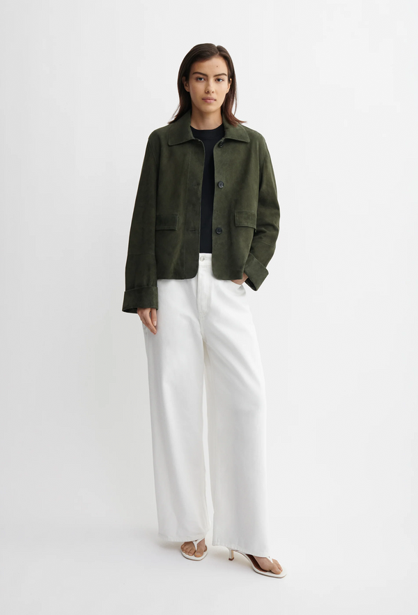 model wearing a green jacket and white pants on a white background