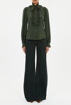 a model wearing a dark green button down blouse with long sleeves, a ruffled neckline and placket, and a necktie. white background.