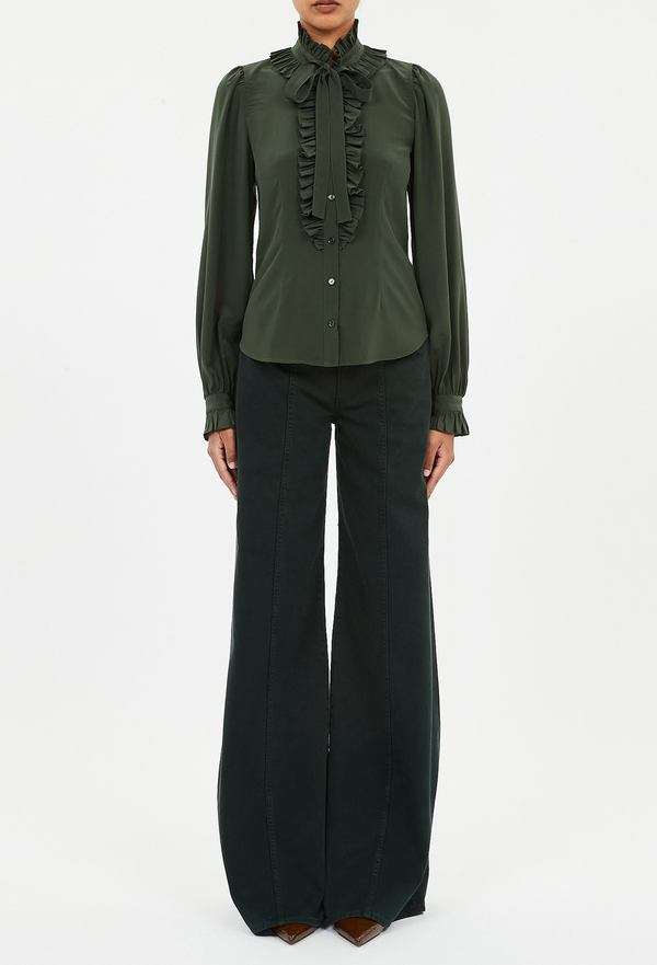a model wearing a dark green button down blouse with long sleeves, a ruffled neckline and placket, and a necktie. white background.