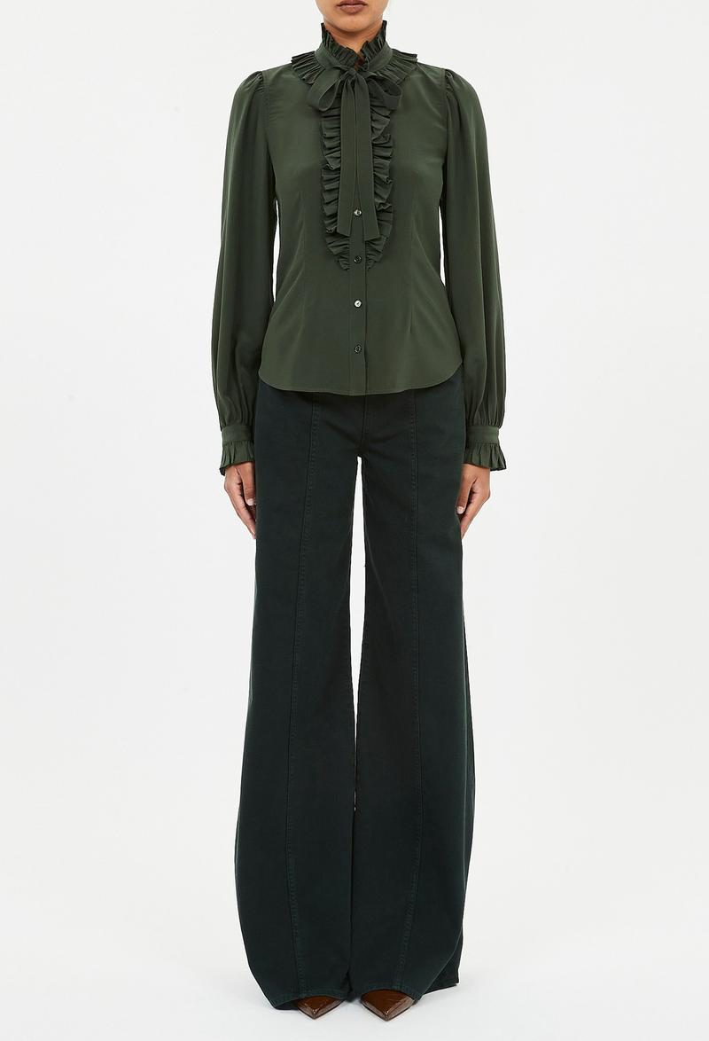 a model wearing a dark green button down blouse with long sleeves, a ruffled neckline and placket, and a necktie. white background.
