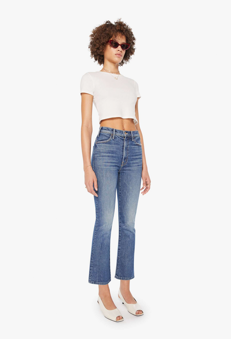 Woman wearing a white crop top and blue cropped jeans on a white background