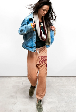 Person wearing a blue denim jacket, orange sweatpants with 'Free City' text, and green sneakers on a white background